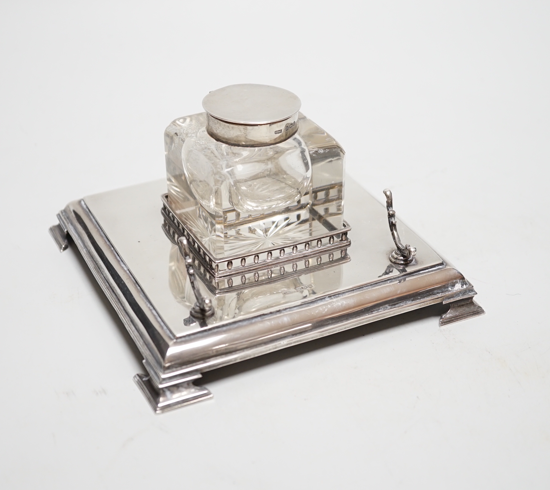 A George V silver inkwell, with mounted glass well and pen rest, James Dixon & Sons, Sheffield, 1928, 15.2cm, base 7.3oz.